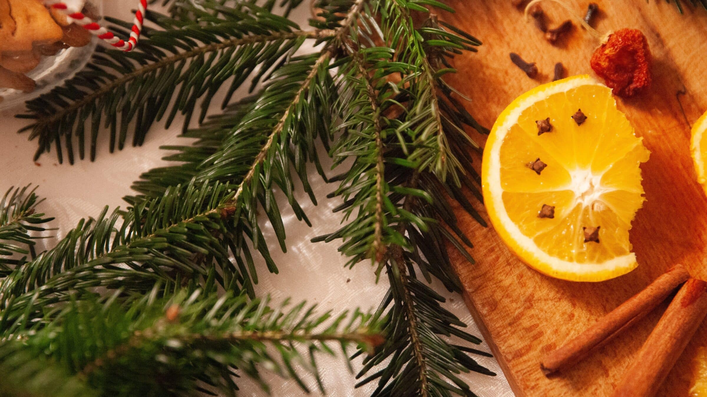 Orange slices, cloves, cinnamon sticks, and evergreen branches artfully laid out on a wooden cutting board